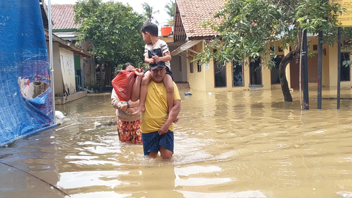 Warga menerjang banjir di wilayah Desa Karangligar, Kecamatan Telukjambe Barat, Kabupaten Karawang, Minggu (2/11/2025). (maemunah/koranmandala)