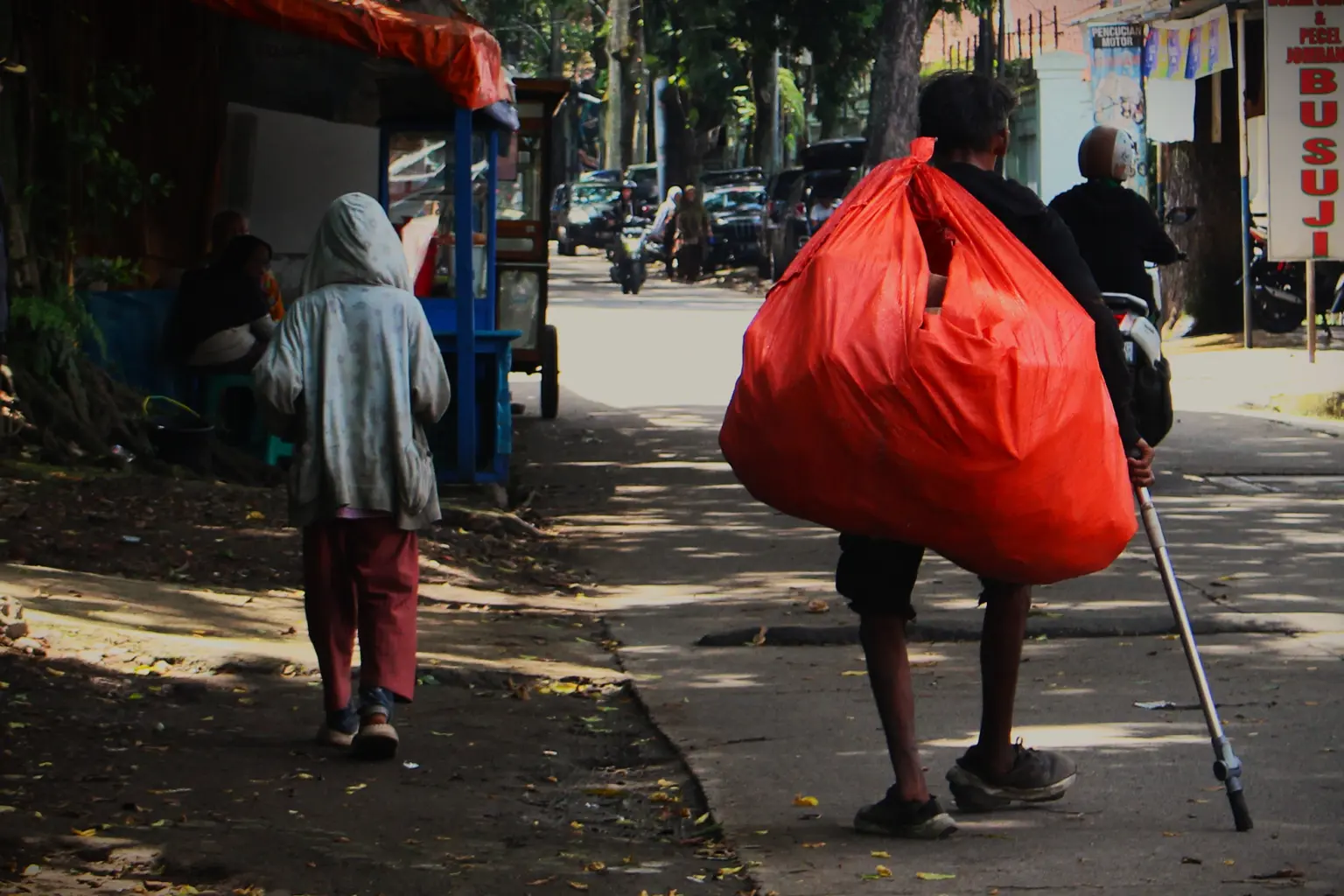 Tunawisma membawa barang bawaan menyusuri jalan kota, Jumat (30/1/2026).