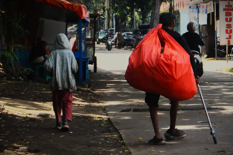 Tunawisma membawa barang bawaan menyusuri jalan kota, Jumat (30/1/2026).