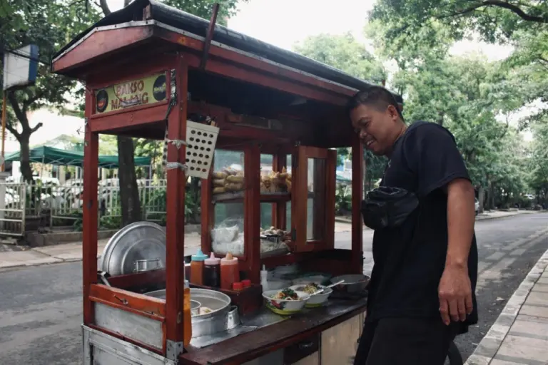 Hujan, Panas, dan Gerobak Bakso: Keteguhan Abdul Mutholib Mencari Rezeki di Jalan Lodaya Pedagang bakso malang tetap semangat berjualan dan terlihat antusias melayani pembeli.(Rifki Rafsanjani)